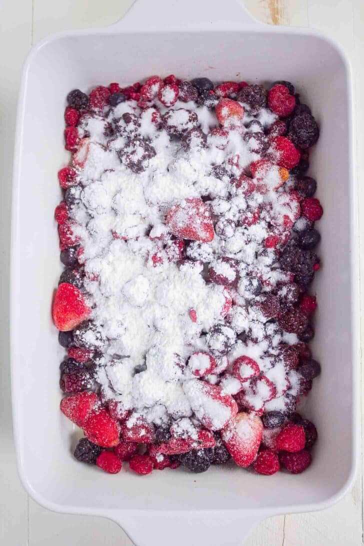 A white baking dish filled with mixed berries and topped with sugar and cornstarch.