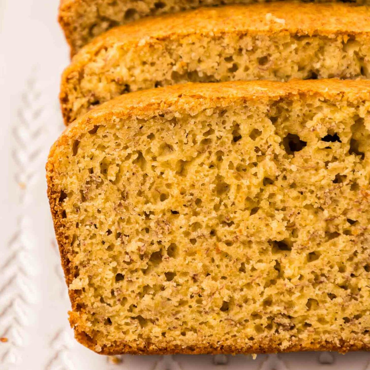 Close-up of sliced cake mix banana bread on a white rectangular plate. The bread has a golden-brown crust and a soft, moist interior with visible banana speckles, showcasing its fluffy texture.