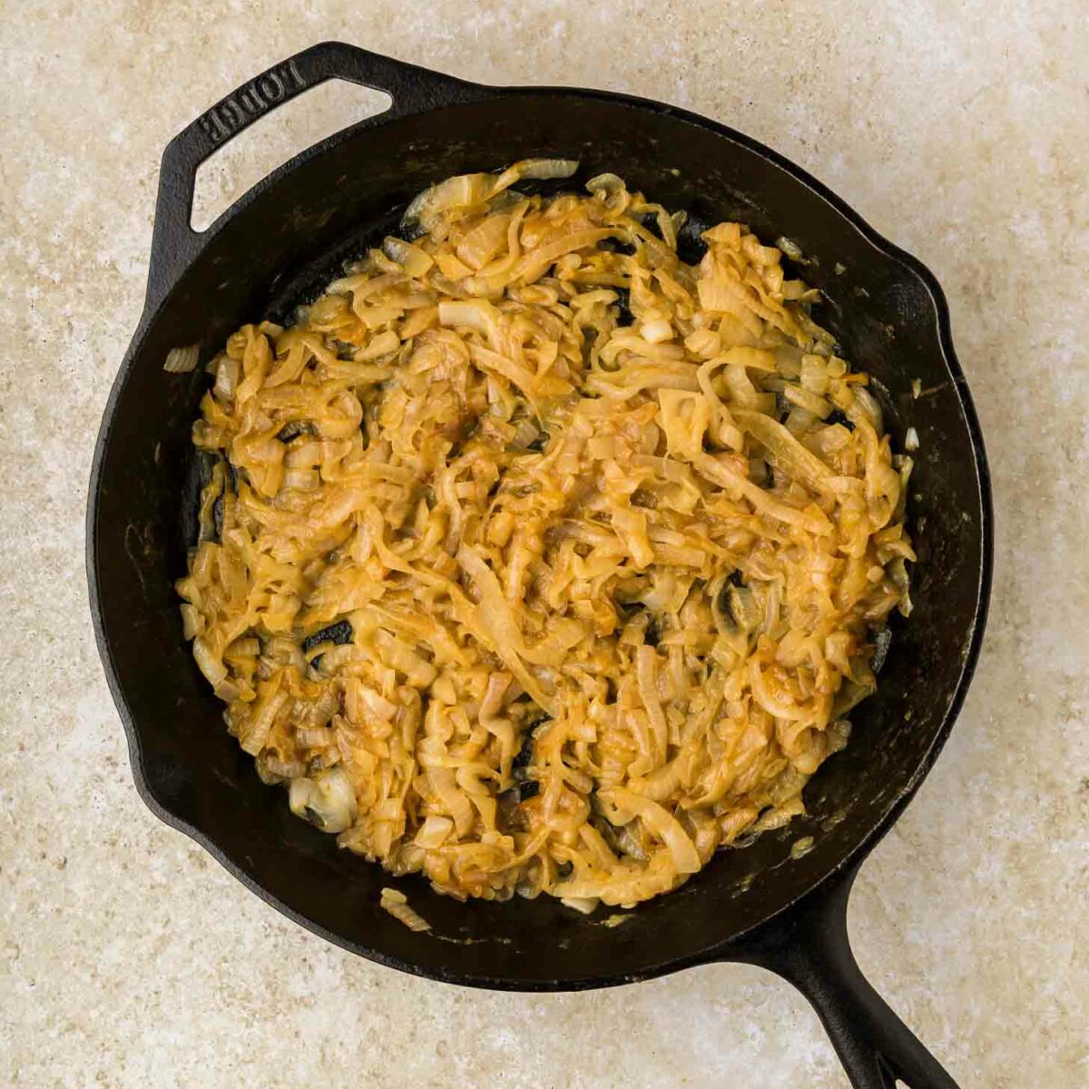 A cast iron skillet filled with golden-brown caramelized onions sits on a light beige countertop.