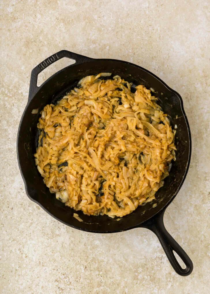 A cast iron skillet filled with golden-brown caramelized onions sits on a light beige countertop.