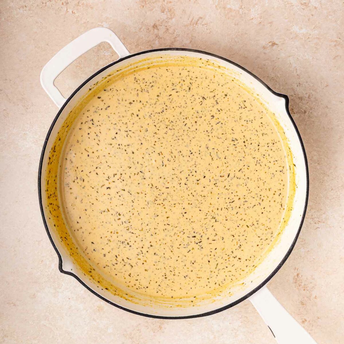 A white skillet filled with a creamy, speckled yellow sauce sits on a light beige countertop.