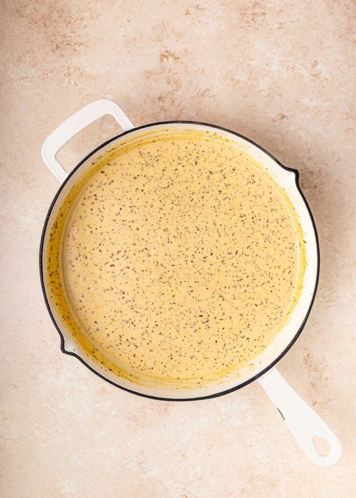 A white skillet filled with a creamy, speckled yellow sauce sits on a light beige countertop.
