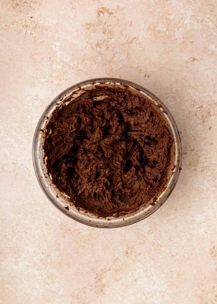 A glass bowl filled with creamy brownie batter sits on a light beige countertop.