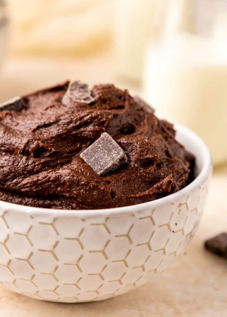 A white bowl with a geometric pattern filled with rich brownie batter, topped with a few chunks of dark chocolate.