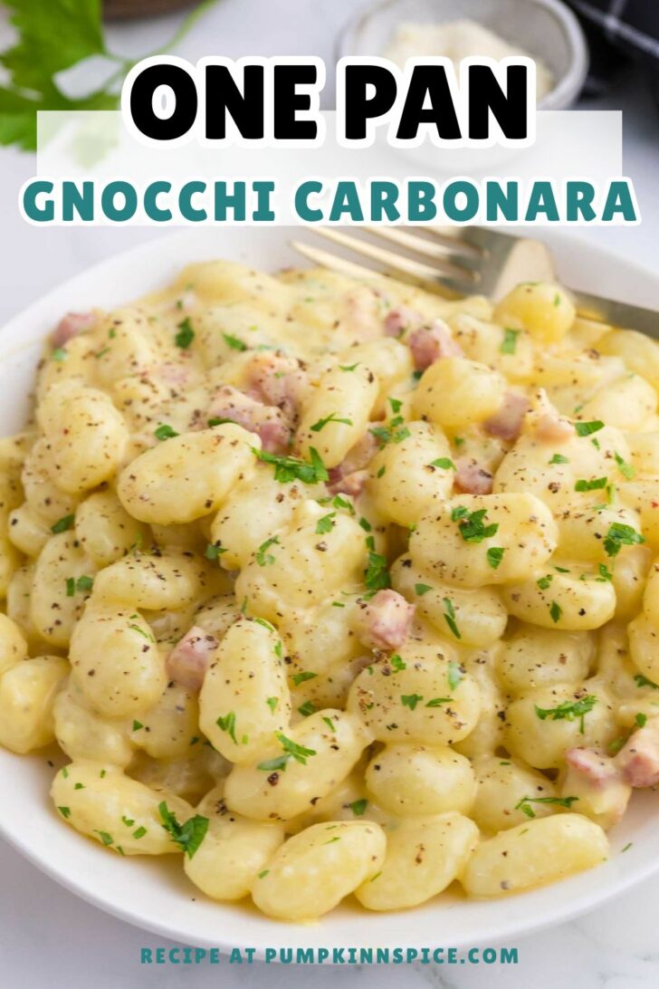 A bowl of creamy gnocchi carbonara topped with diced pancetta, black pepper, and parsley. A fork rests in the bowl, and the text reads One Pan Gnocchi Carbonara with a recipe link at the bottom.