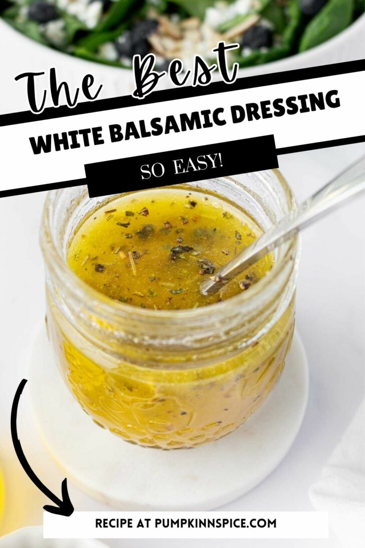 A small glass jar of white balsamic dressing with herbs, a spoon inside, sits on a white plate. Text on the image reads, The Best White Balsamic Dressing—So Easy! Recipe at pumpkinnspice.com.