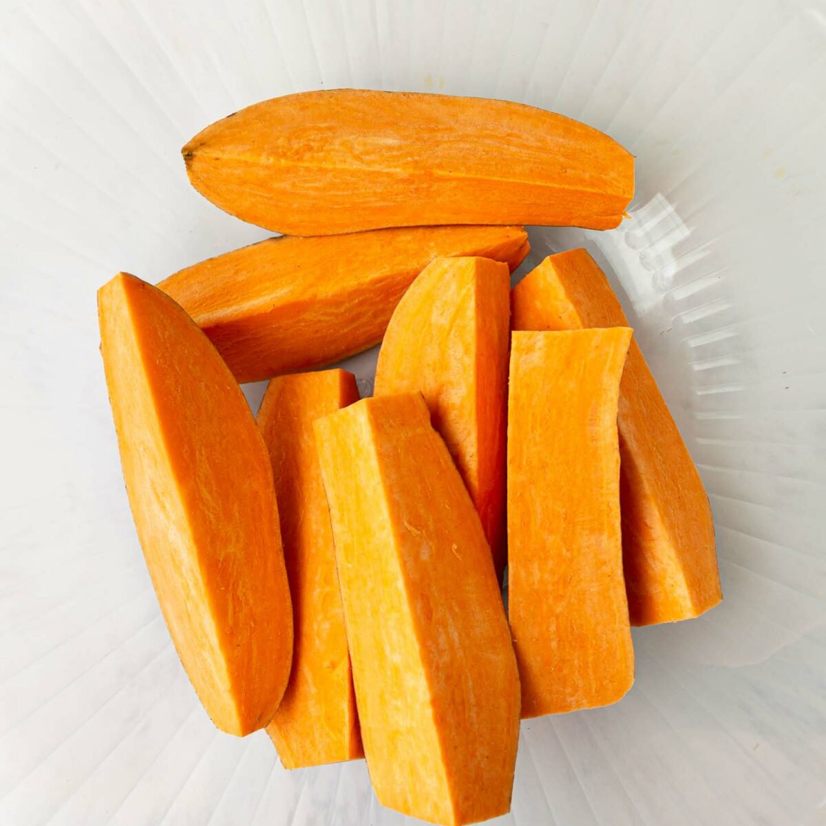 Peeled and sliced sweet potatoes arranged in a clear glass bowl, seen from above.
