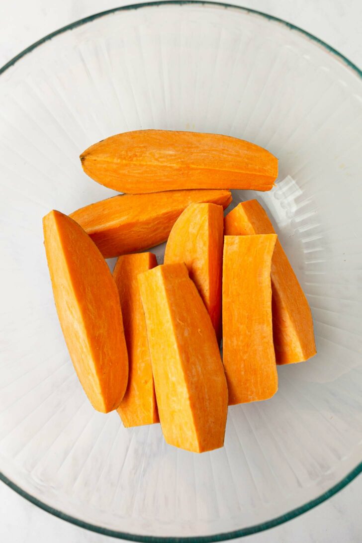 Peeled and sliced sweet potatoes arranged in a clear glass bowl, seen from above.
