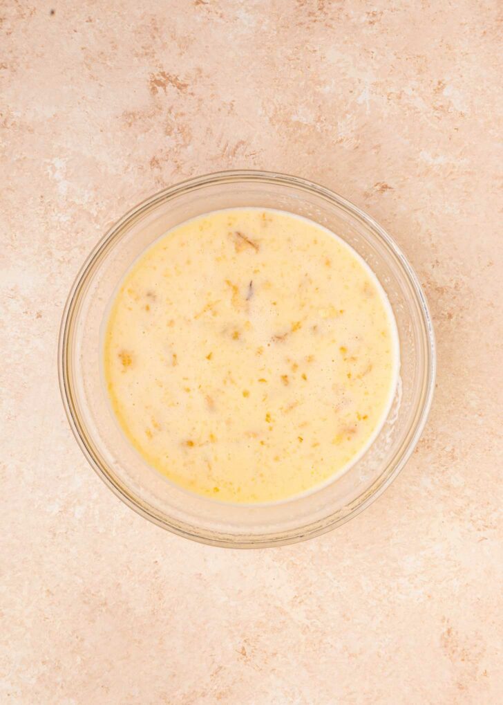 A glass bowl filled with a creamy, speckled egg mixture sits on a light beige countertop viewed from above.