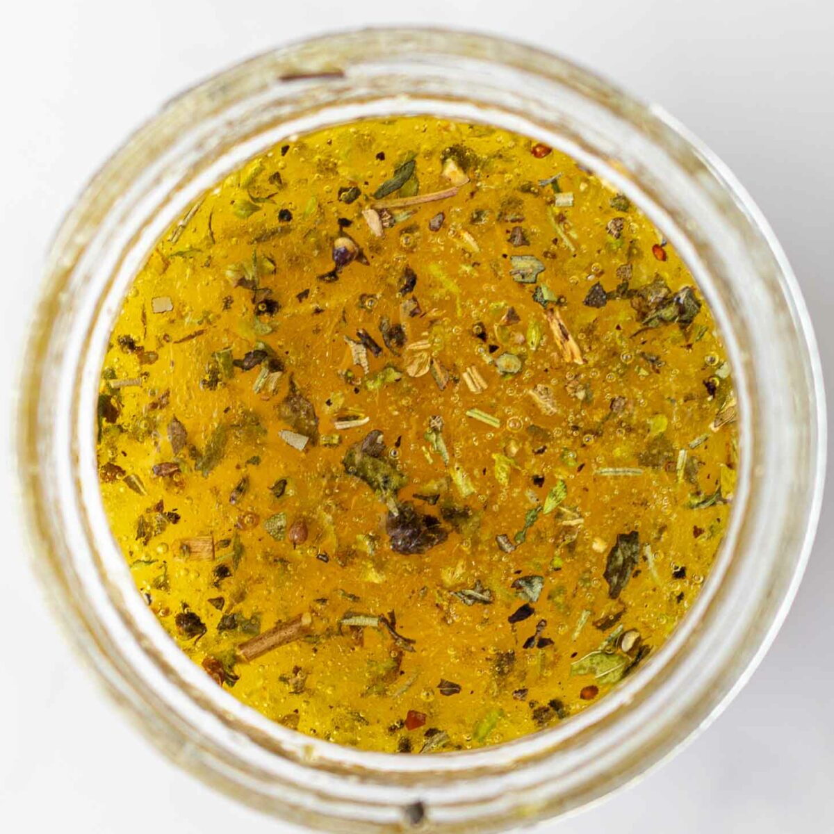 A top-down view of a jar filled with dressing mixed with herbs and spices, set against a light background.