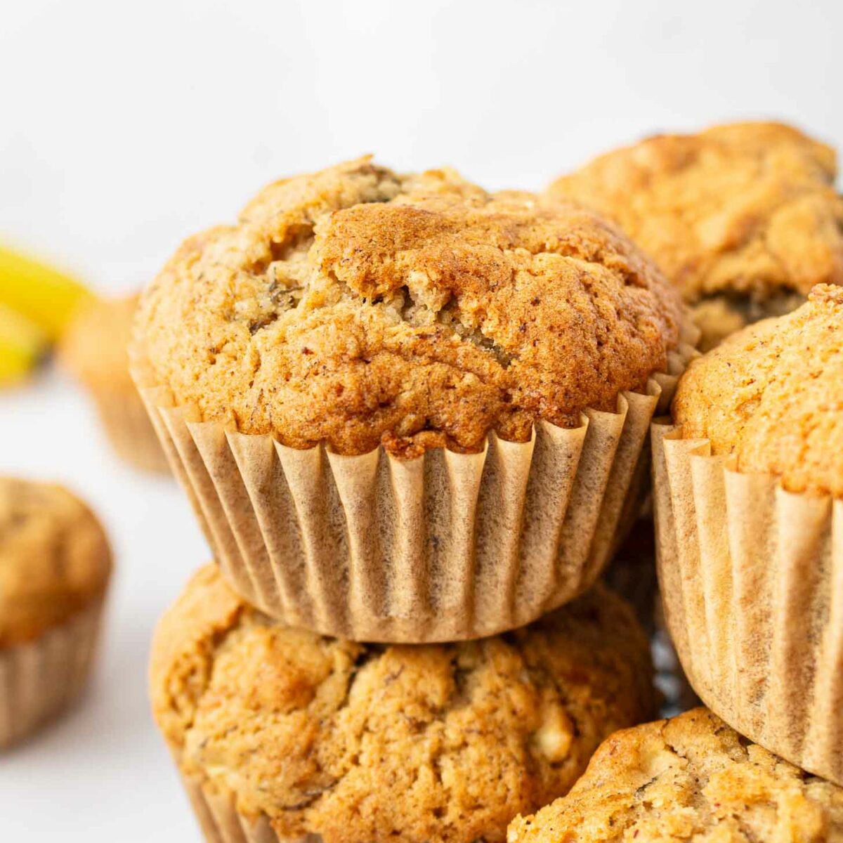 Close-up of golden brown muffins stacked on a black wire rack, with a light background and a few more muffins visible in the background.