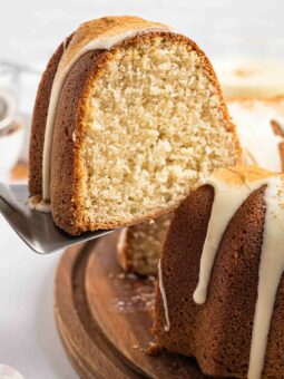 A close-up of a sliced eggnog pound cake with a golden-brown crust and moist, light interior, topped with a drizzle of white icing, served on a wooden board.