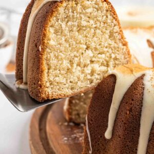 A close-up of a sliced eggnog pound cake with a golden-brown crust and moist, light interior, topped with a drizzle of white icing, served on a wooden board.