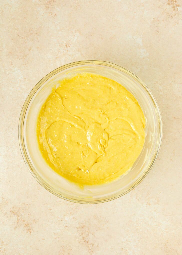 A clear glass bowl filled with yellow cake batter sits on a light beige countertop.