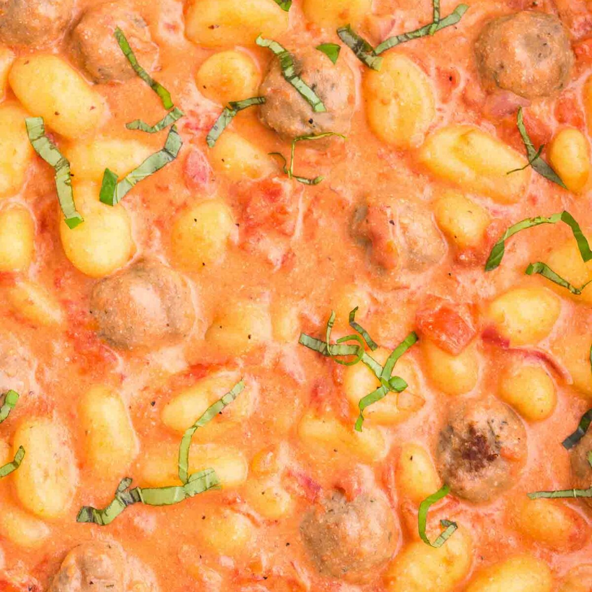 Gnocchi and meatballs in a creamy tomato sauce, garnished with fresh basil, shown in a close-up view.