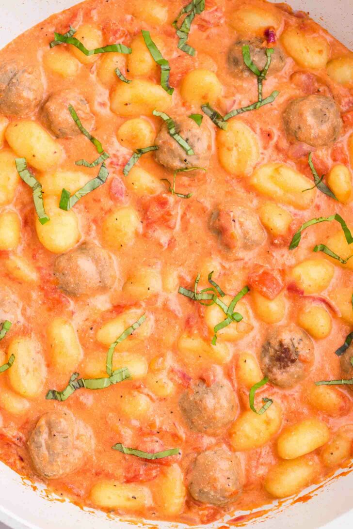 Gnocchi and meatballs in a creamy tomato sauce, garnished with fresh basil, shown in a close-up view.