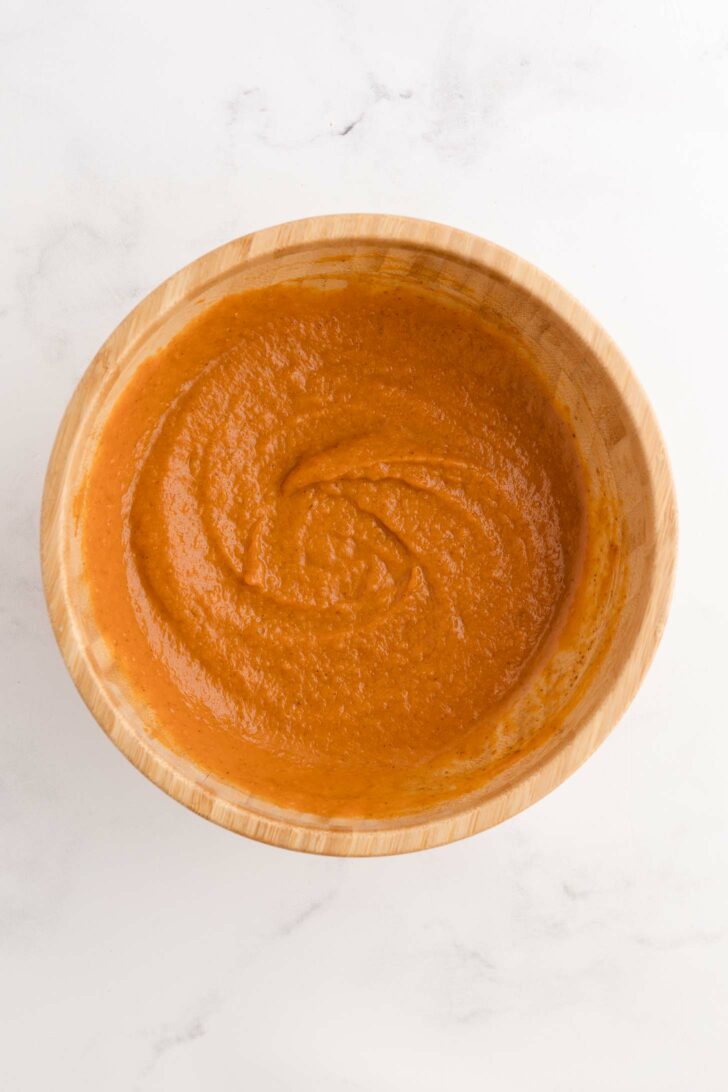A wooden bowl filled with smooth, orange-pumpkin mixture, placed on a white marble surface.