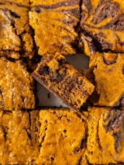 Close-up of pumpkin swirl brownies cut into squares, with one piece slightly raised to show the marbled layers of dark chocolate and orange pumpkin batter.