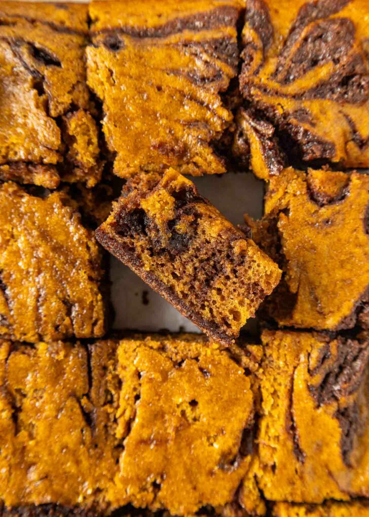 Close-up of pumpkin swirl brownies cut into squares, with one piece slightly raised to show the marbled layers of dark chocolate and orange pumpkin batter.