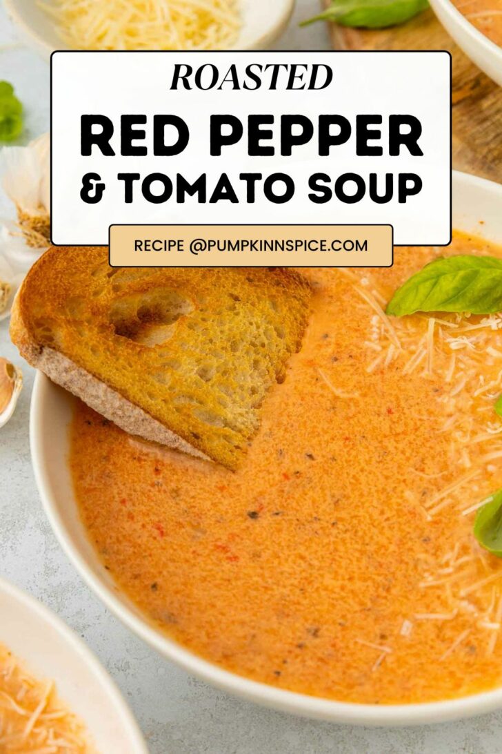 A bowl of creamy roasted red pepper and tomato soup topped with shredded cheese and a slice of toasted bread, garnished with fresh basil leaves. Text overlay reads: Roasted Red Pepper & Tomato Soup.