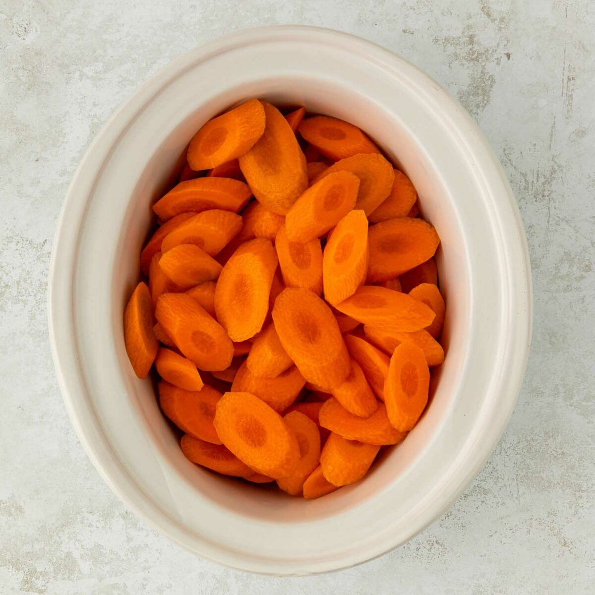 A white bowl filled with sliced carrots placed on a light textured surface.