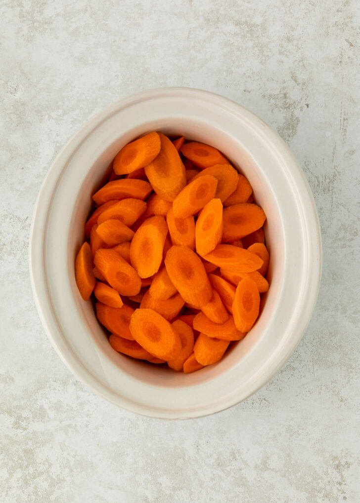 A white bowl filled with sliced carrots placed on a light textured surface.