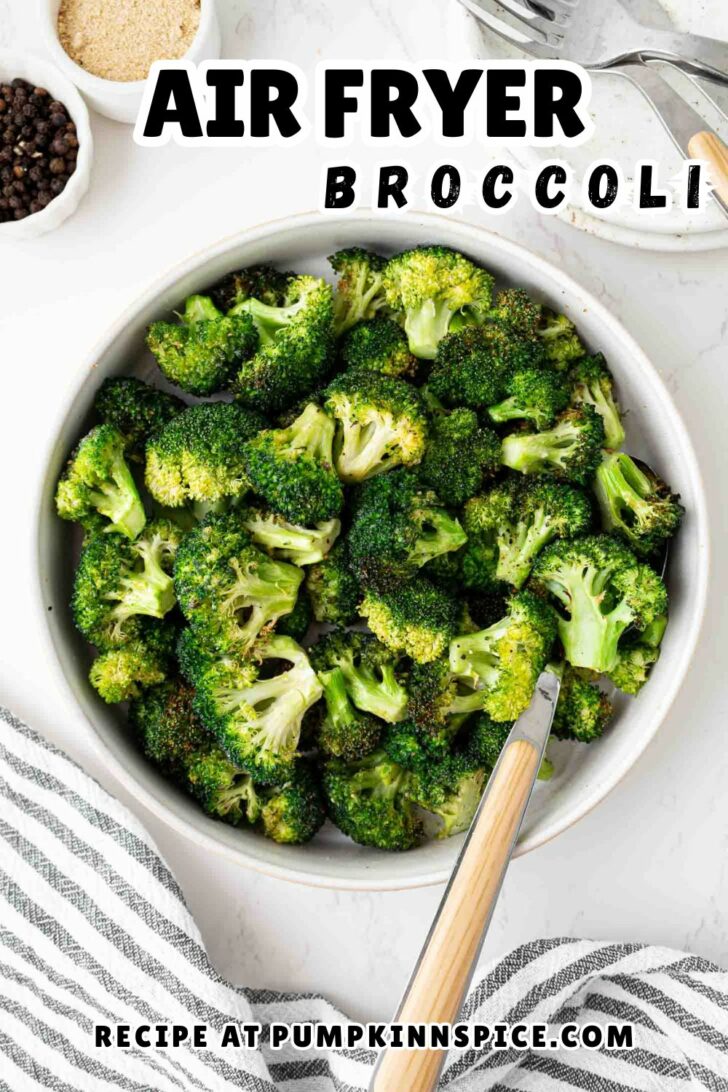 A bowl filled with cooked broccoli florets sits on a white table with a fork resting inside. Text overlay reads Air Fryer Broccoli. The bottom text says Recipe at pumpkinnspice.com.