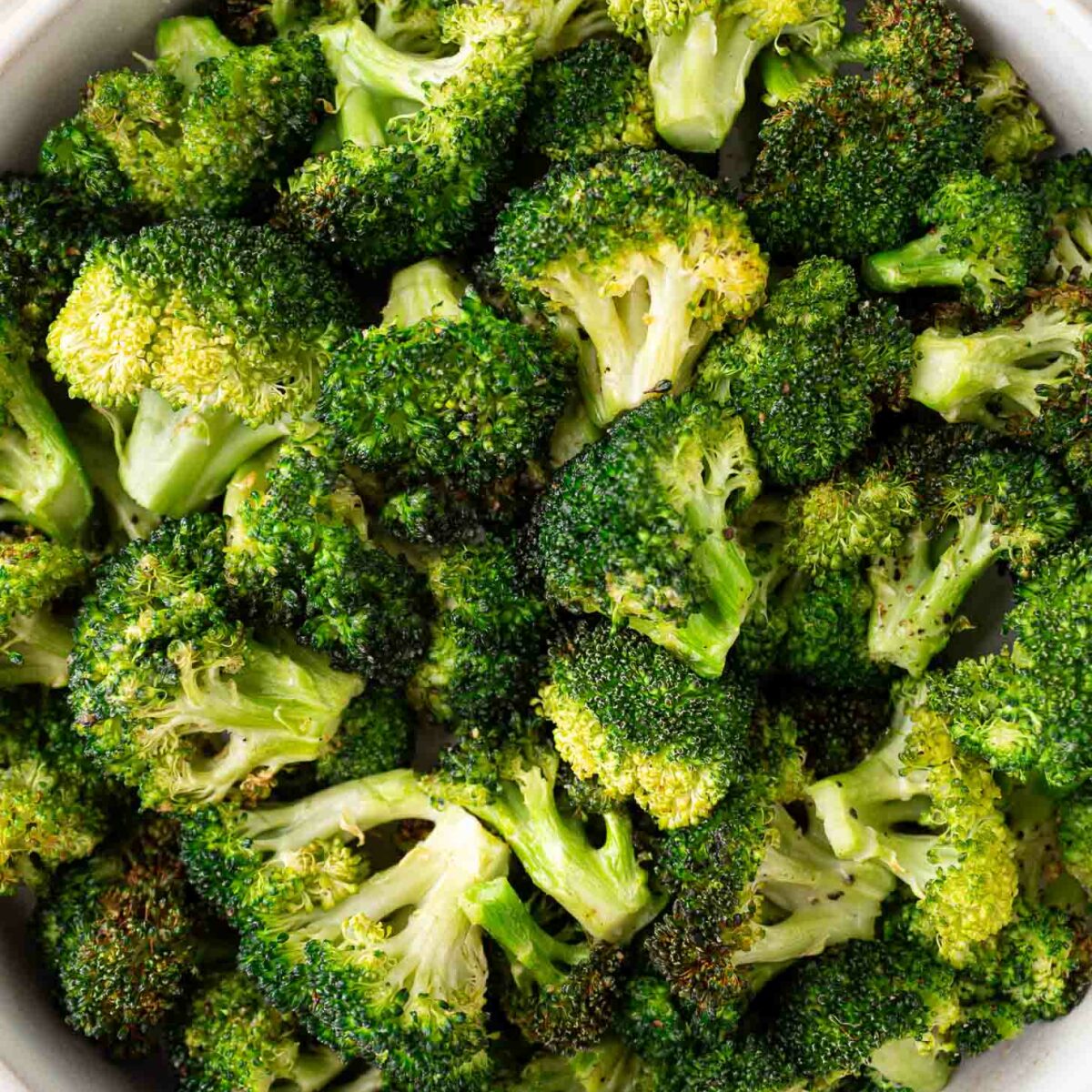 A bowl filled with roasted broccoli florets, showing crispy, browned edges and vibrant green color.