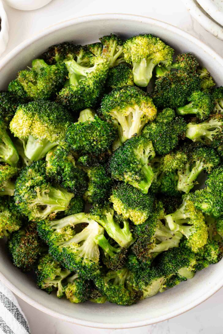 A bowl filled with roasted broccoli florets, showing crispy, browned edges and vibrant green color.