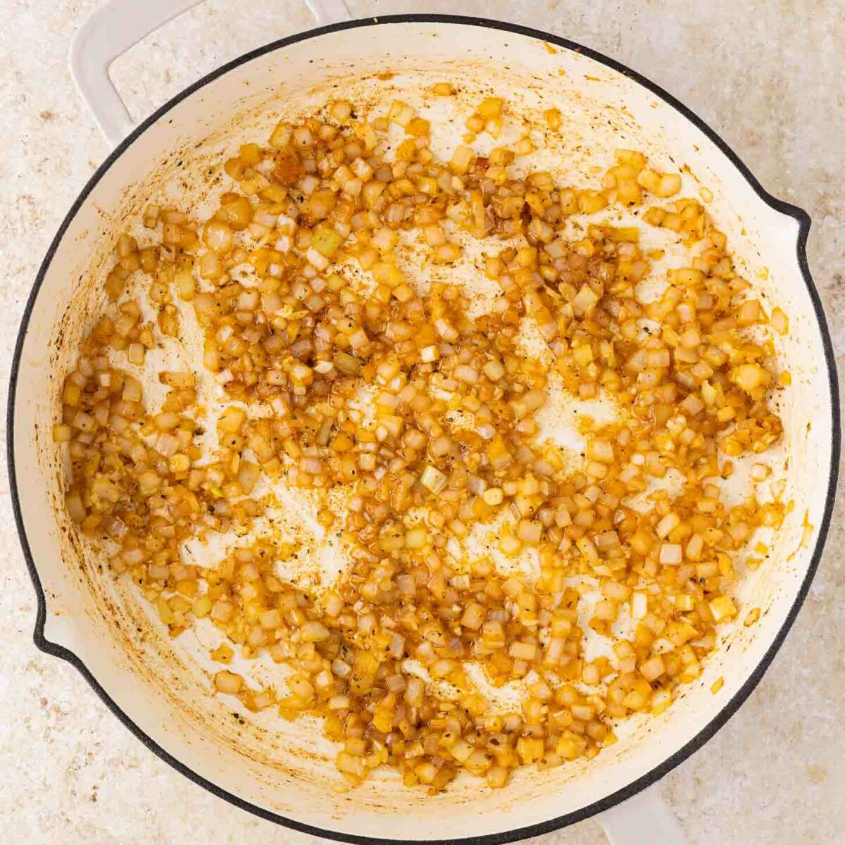 A white skillet with sautéed diced onions, lightly browned and caramelized, set on a light-colored countertop.