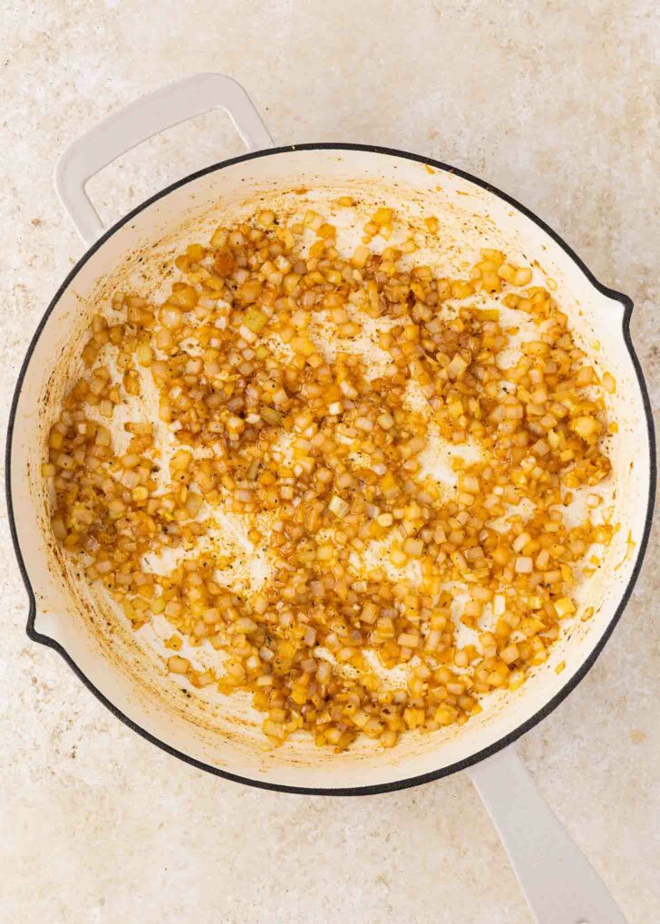 A white skillet with sautéed diced onions, lightly browned and caramelized, set on a light-colored countertop.