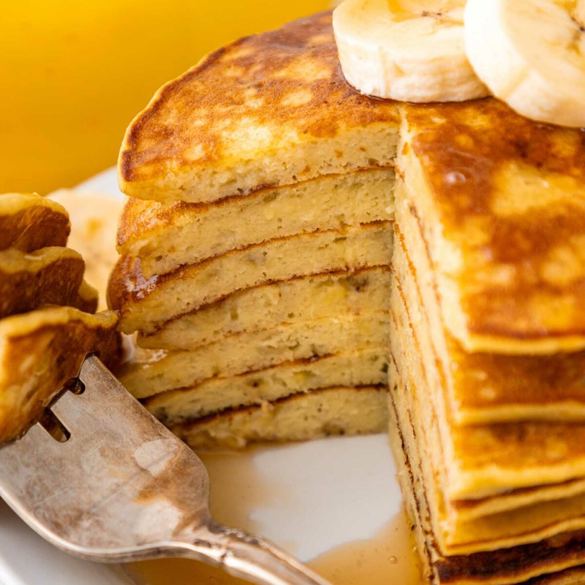 A stack of banana pancakes with bananas and syrup.