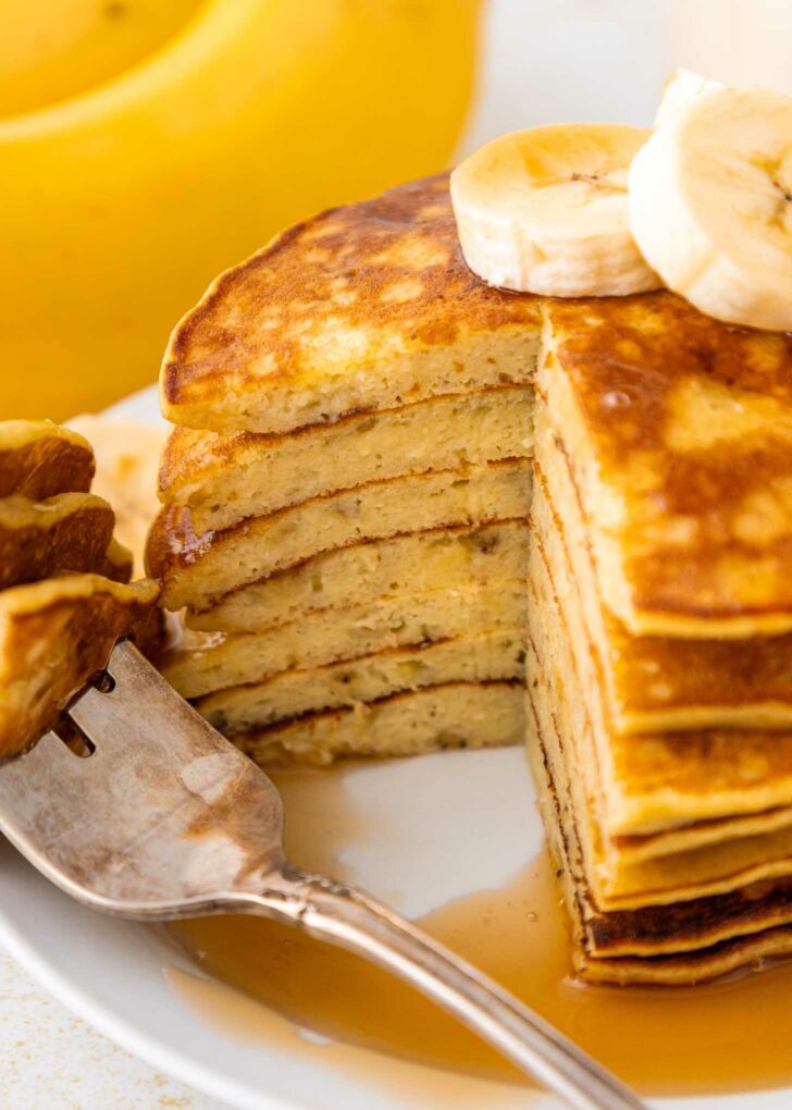 A stack of banana pancakes with bananas and syrup.