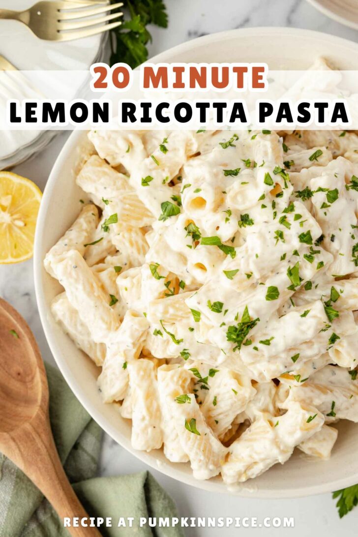 A bowl of creamy lemon ricotta pasta garnished with chopped parsley. There is a wooden spoon, half a lemon, and a fork nearby. Text on the image reads 20 Minute Lemon Ricotta Pasta and Recipe at pumpkinnspice.com.