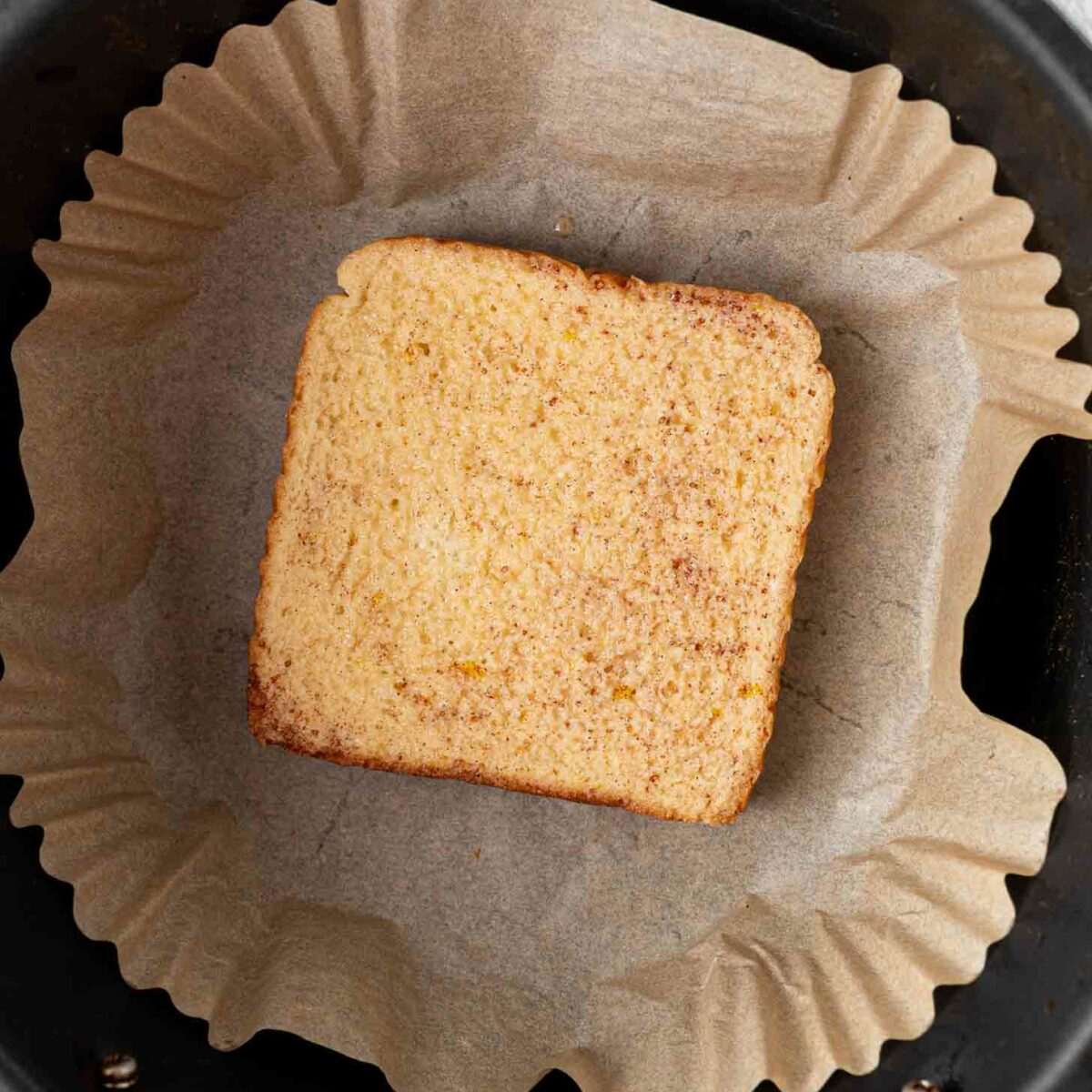 A slice of soaked bread sits on a piece of brown parchment paper inside an air fryer basket.
