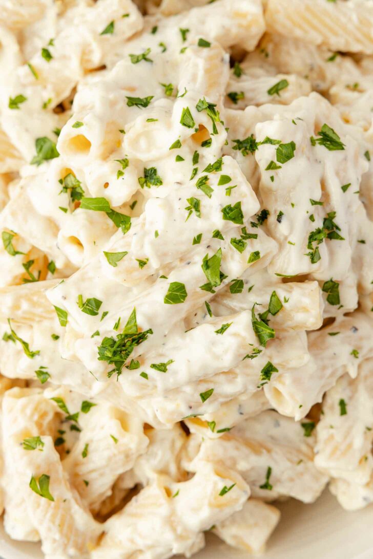 Close-up of creamy rigatoni pasta covered in a white sauce, garnished with chopped fresh parsley.