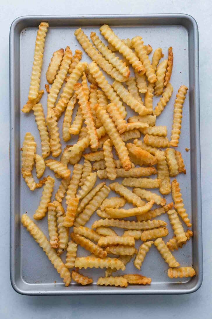 A baking sheet covered with a scattered layer of crispy, golden crinkle-cut French fries.