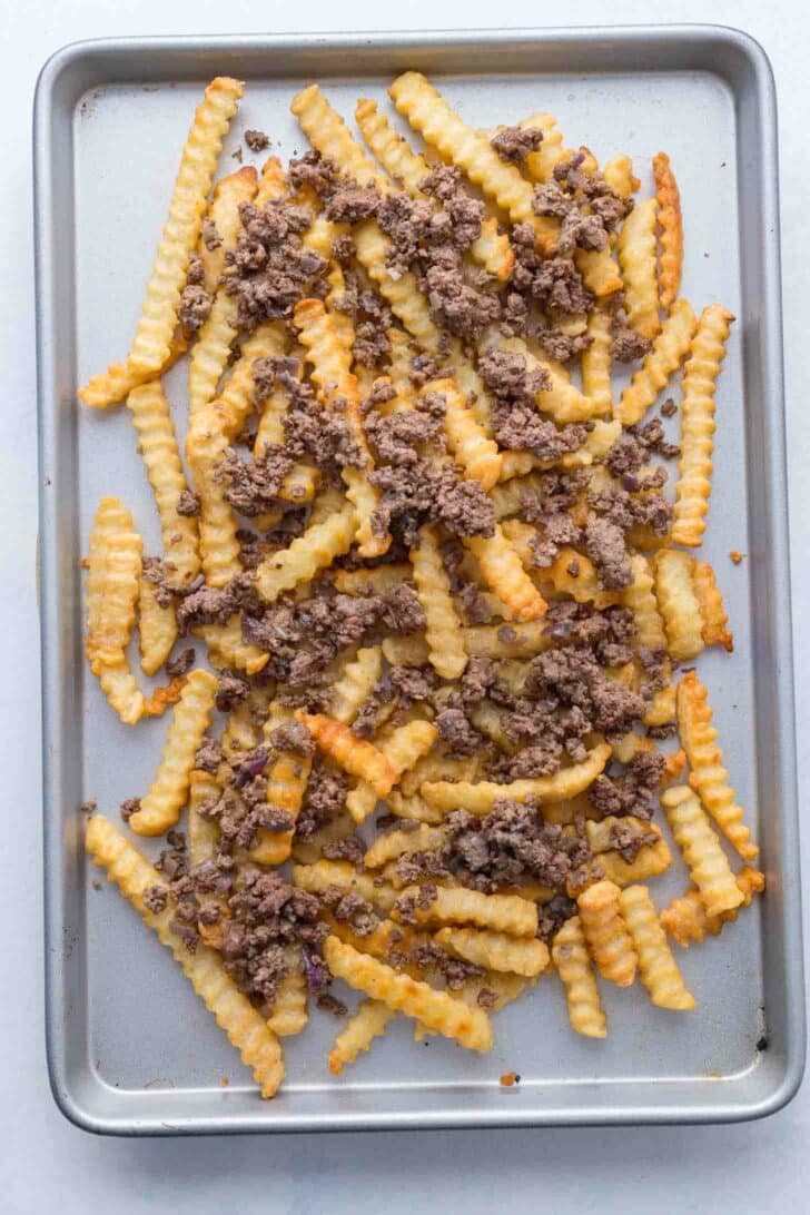 A baking sheet topped with crinkle-cut French fries and browned ground beef scattered over them.