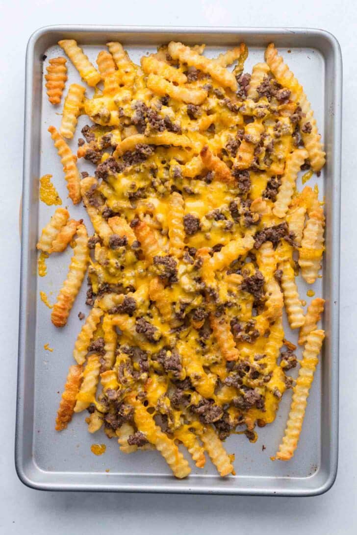 A baking sheet topped with crinkle-cut French fries, cooked ground beef, and melted cheddar cheese, creating a loaded fries dish.