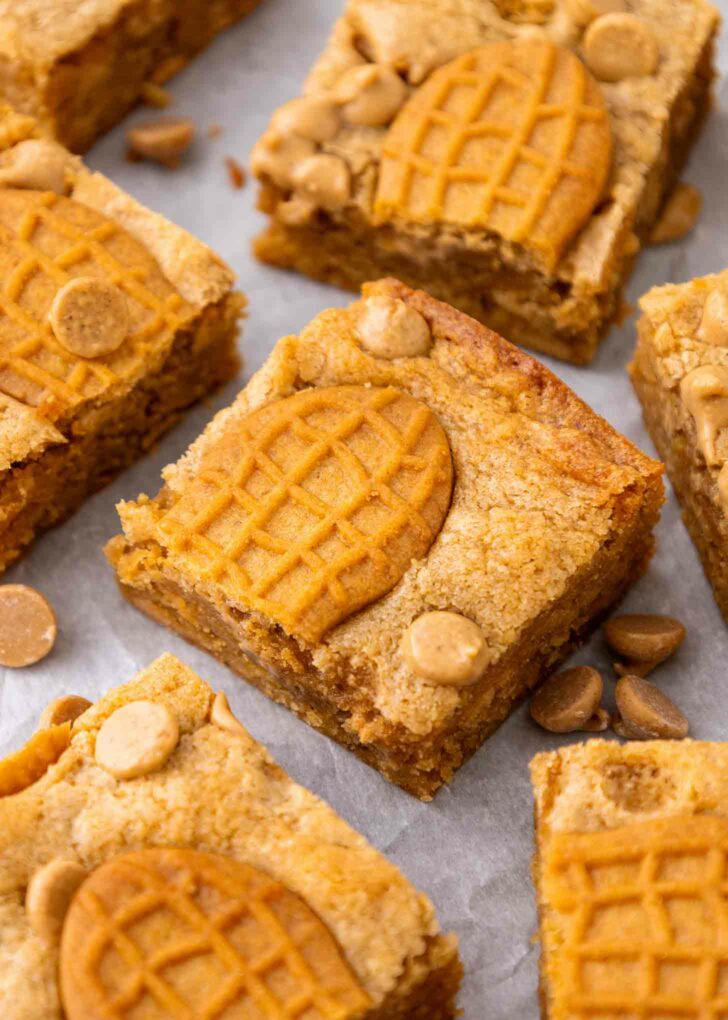 Close-up of peanut butter bars topped with peanut-shaped cookies and peanut butter chips, arranged on parchment paper.