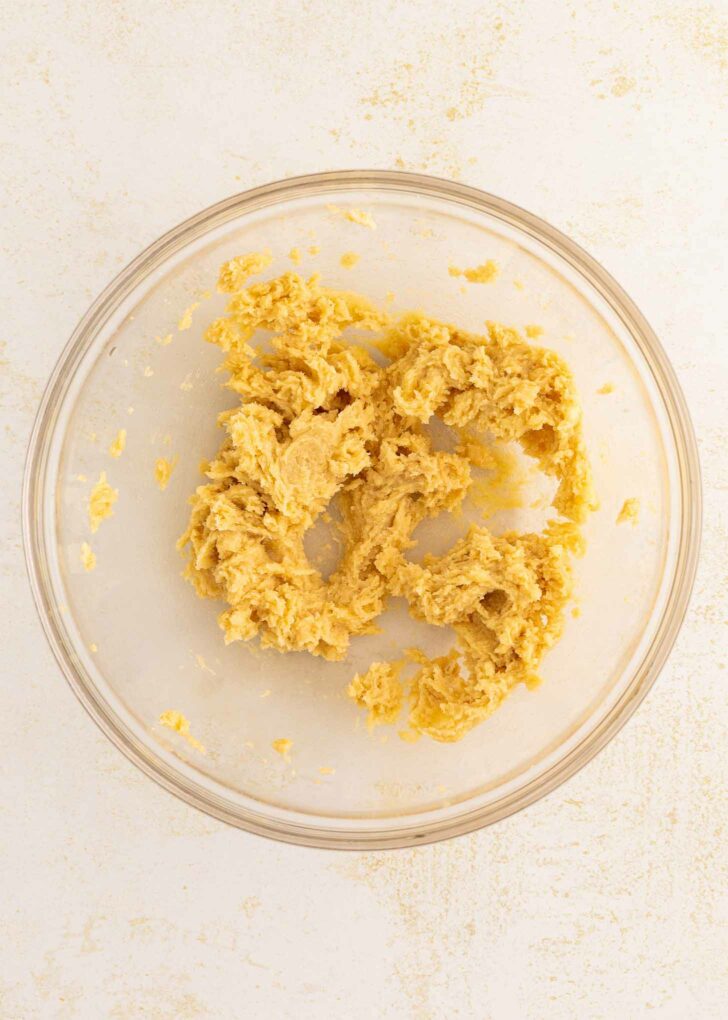 A glass mixing bowl containing partially mixed dough sits on a light-colored countertop.