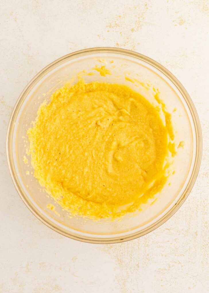 A clear glass bowl filled with a yellow, slightly lumpy batter sits on a light-colored countertop.