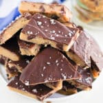 A bowl filled with pieces of cookie dough bark topped with sea salt. The dough has a thick chocolate layer and is arranged in a stacked pile on a white plate.