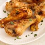 A white plate with several air fryer chicken drumsticks garnished with chopped fresh parsley. The chicken has a golden-brown, crispy exterior.
