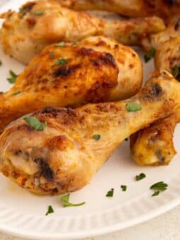 A white plate with several air fryer chicken drumsticks garnished with chopped fresh parsley. The chicken has a golden-brown, crispy exterior.