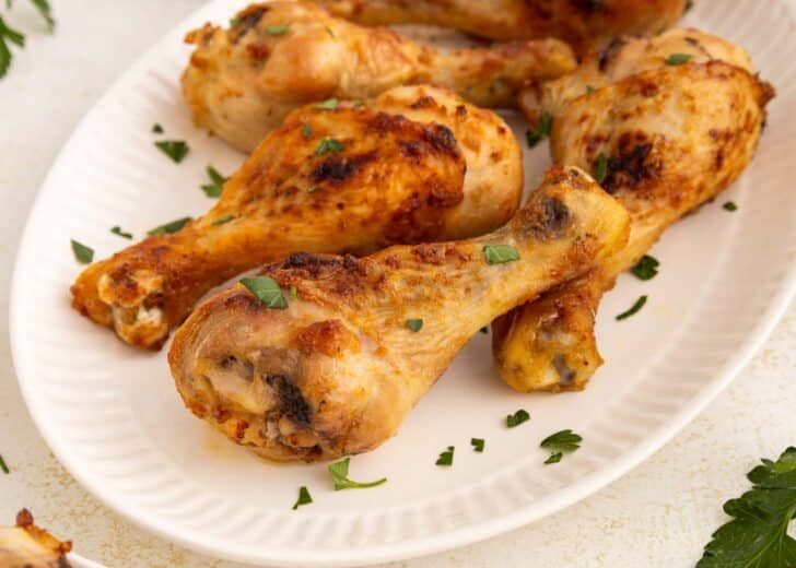 A white plate with several air fryer chicken drumsticks garnished with chopped fresh parsley. The chicken has a golden-brown, crispy exterior.