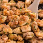 Golden brown, seasoned chicken pieces being sautéed in a pan with a spatula, garnished with chopped herbs.