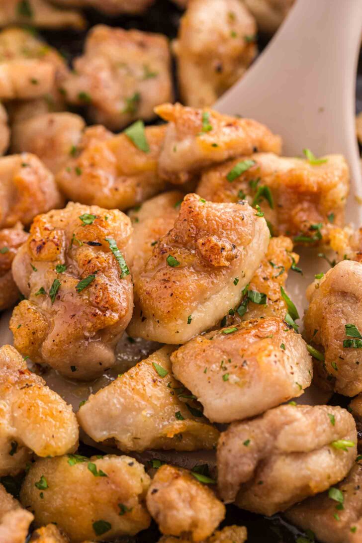 Close-up of golden-brown, pan-seared chicken pieces garnished with chopped parsley, served on a beige spatula.