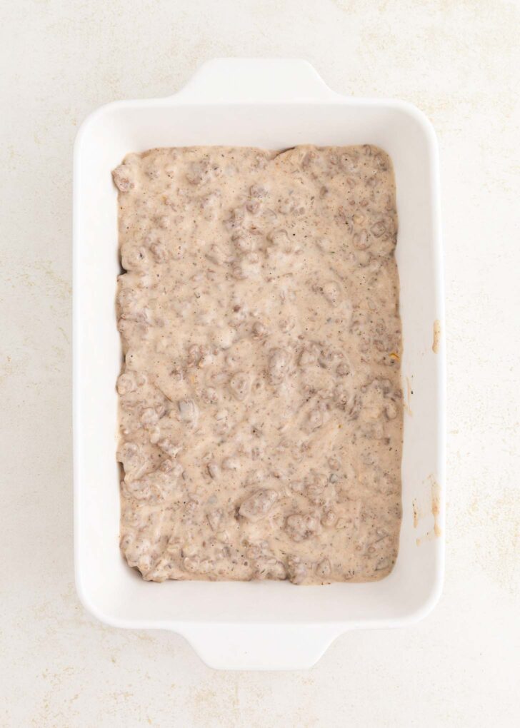 A white rectangular baking dish filled with a thick, creamy mixture containing small chunks of ground meat and sauce, spread evenly across the bottom.