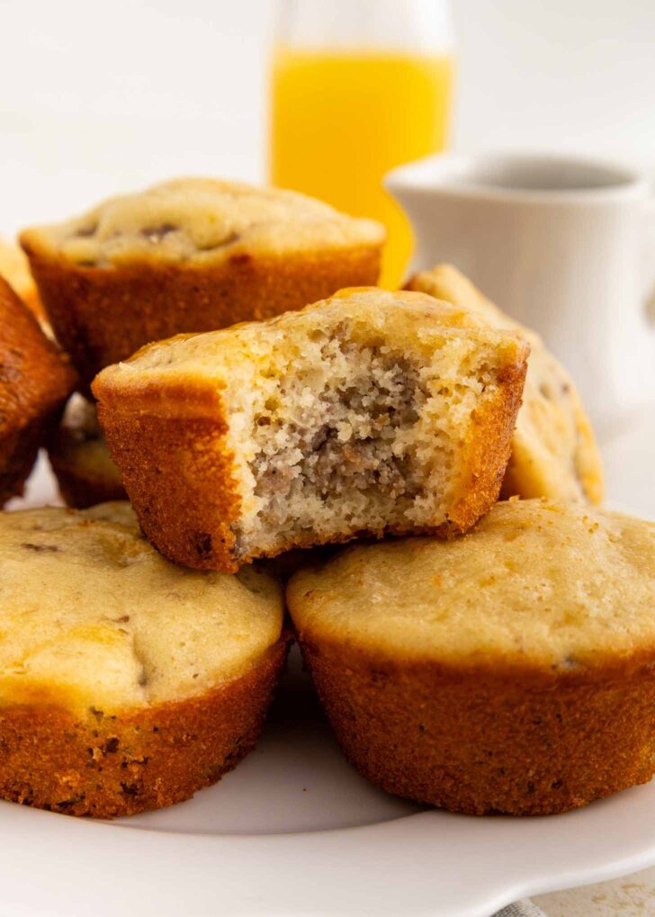 A close-up of mcgriddle muffins on a white plate, with one muffin showing a bite taken out. In the background, there is a glass of orange juice and a white pitcher.